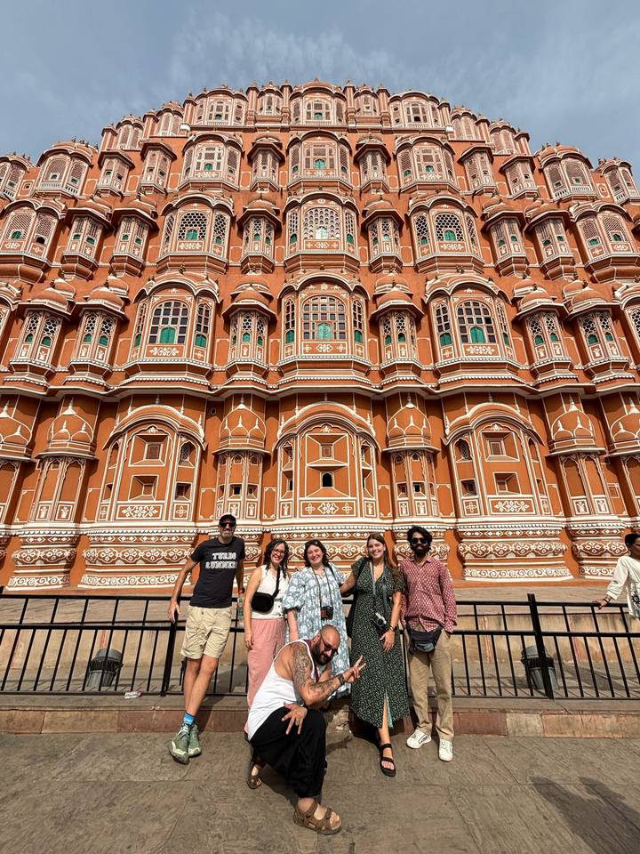A group of travelers stands before the ornate red-sandstone façade of Jaipur’s Hawa Mahal under a clear sky.