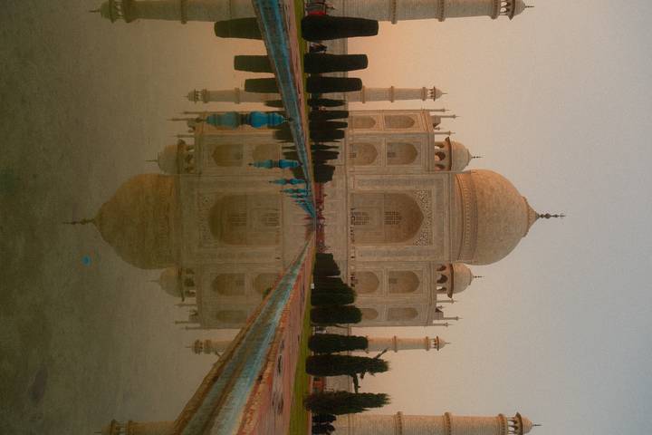 The Taj Mahal glows softly at dawn, perfectly mirrored in the long reflecting pool leading to the mausoleum.