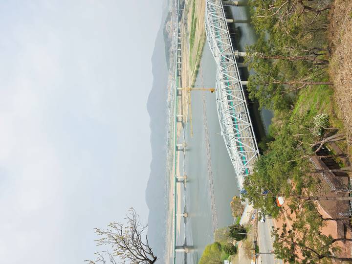Multiple bridges crossing a wide river flanked by rolling hills and sparse development under hazy light.