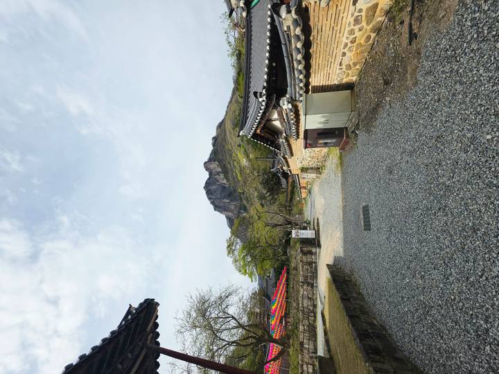 Gravel pathway between traditional Korean walls leading toward a rocky mountain peak under soft clouds.