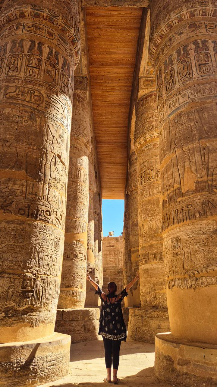 Massive sandstone columns filled with hieroglyphics at an ancient Egyptian temple with blue sky framed overhead.