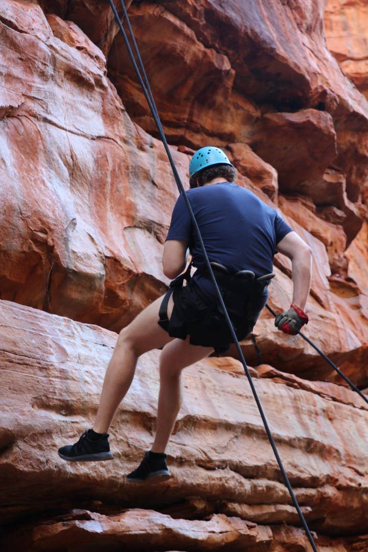 Adventurer rappels down red sandstone cliffs wearing safety harness and gloves.