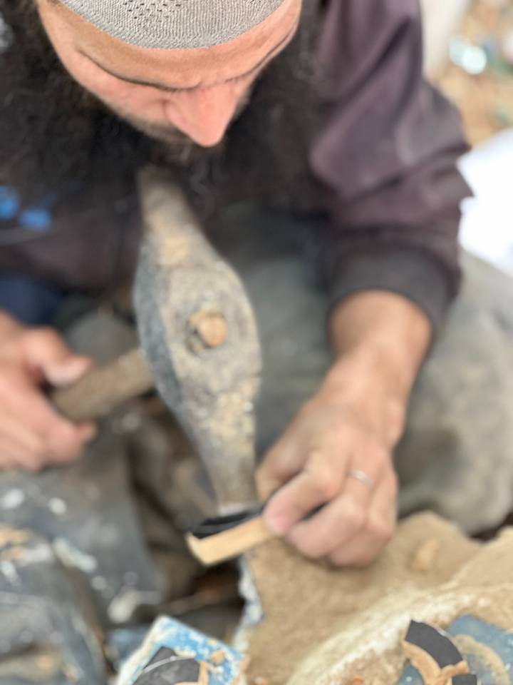 Blurry close-up of a person hammering a piece of metal with a worn tool.