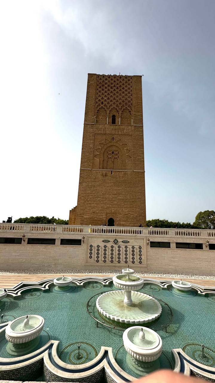 Tall sandstone Hassan Tower rises above a white marble terrace with visitors
