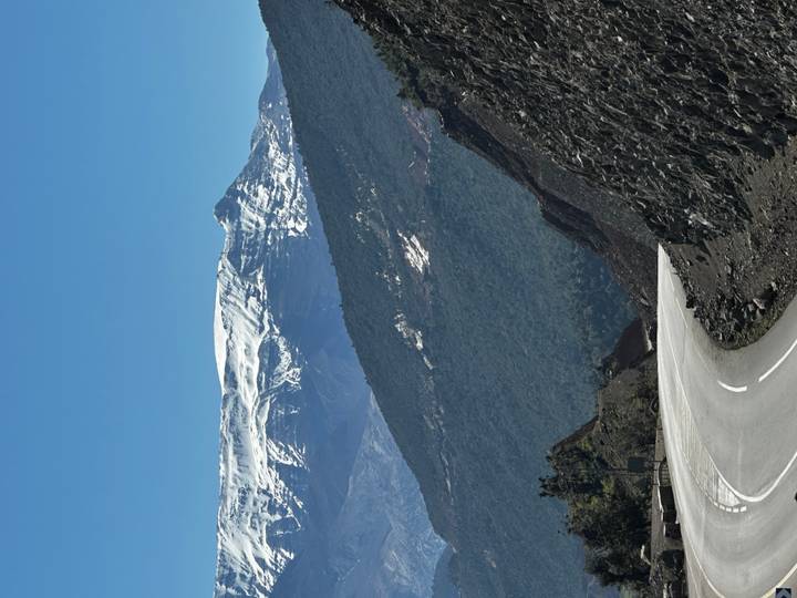 Winding mountain road leads toward snow-capped peaks under a deep blue sky