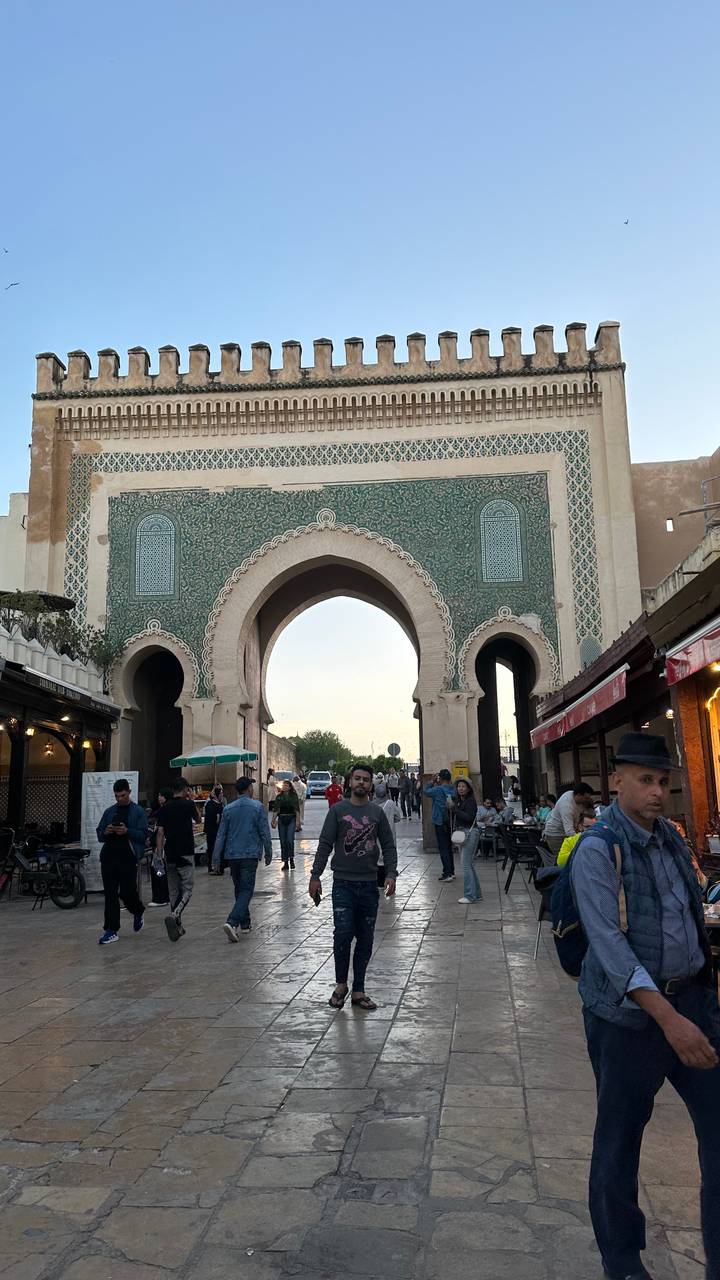 Crowds pass through the ornate green-tiled Bab Boujloud gate at dusk