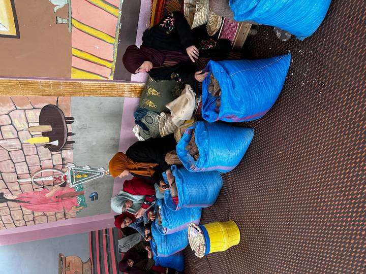 Local women in scarves sort argan nuts into bright blue sacks indoors