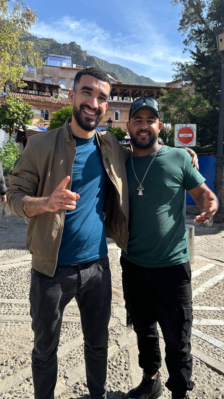 Two smiling friends pose arm-in-arm on a sunny street