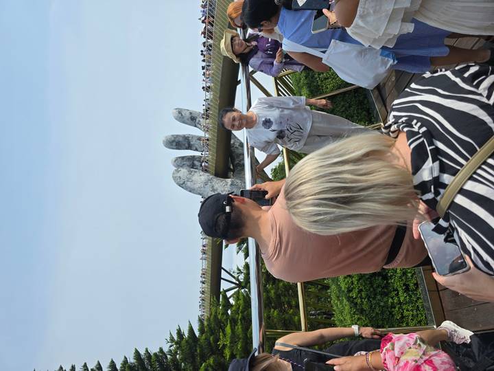 Crowds photograph a woman posing in front of the giant hand-supported Golden Bridge high in the mountains.