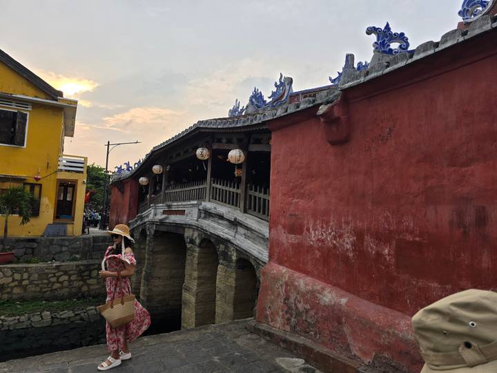 A traveler in a straw hat walks beside the historic wooden Japanese Covered Bridge at dusk.