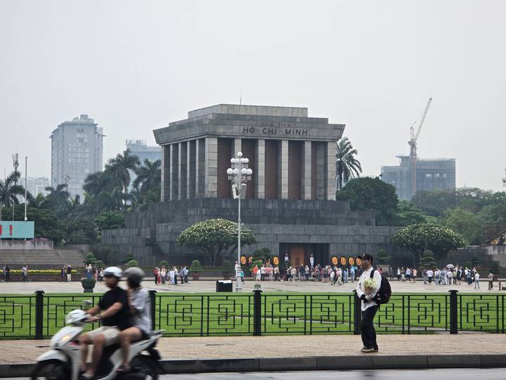 Visitors gather in front of the imposing gray stone Ho Chi Minh Mausoleum on an overcast day.