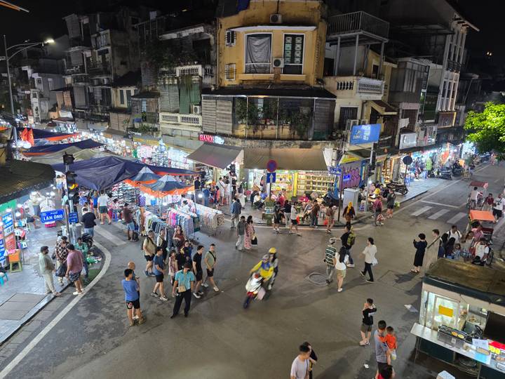 A vibrant night market buzzes with shoppers under bright stall lights in Hanoi's Old Quarter.