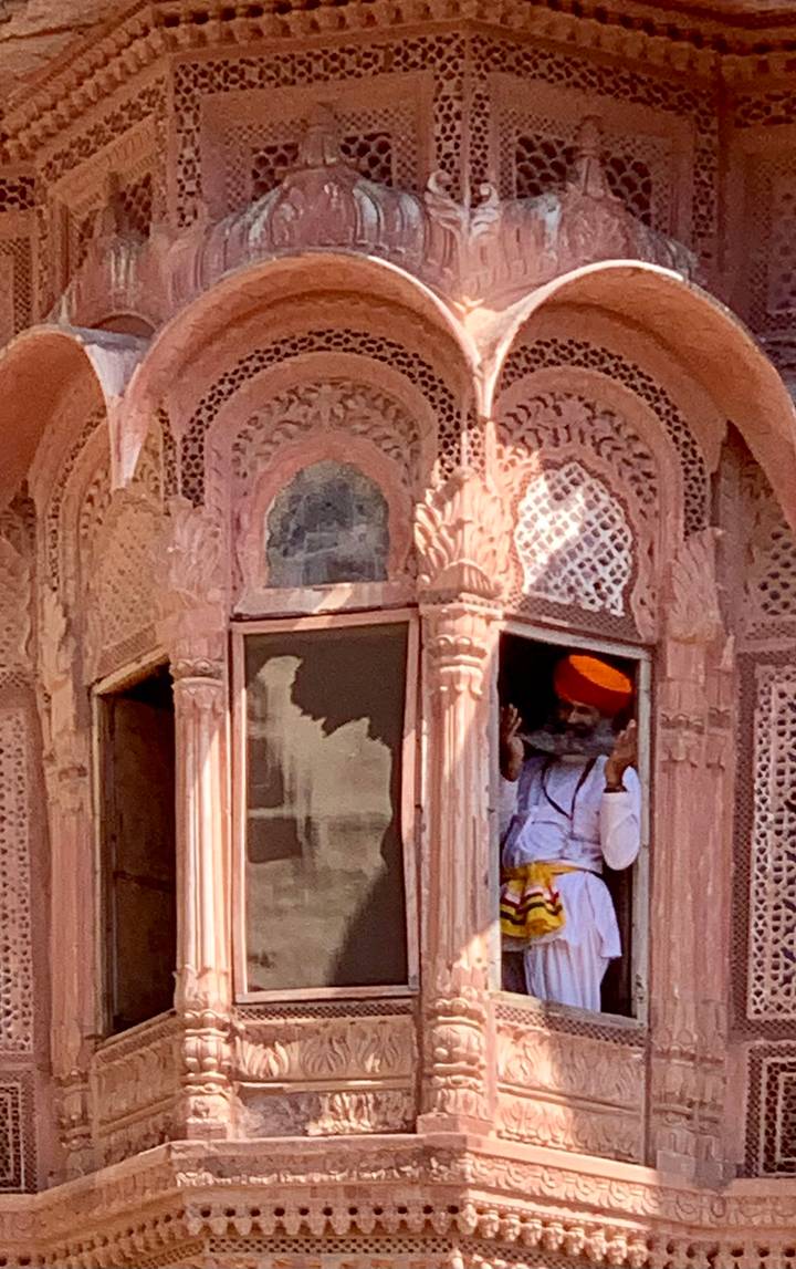 Man in orange turban peers from intricately carved pink sandstone window