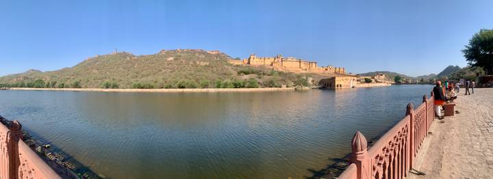 Hilltop fort complex overlooking a calm lake and surrounding arid hills under clear blue sky.