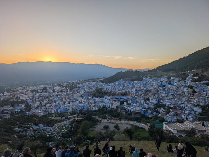 Wide sunset panorama of a mountain-ringed valley town with distinctive blue buildings.