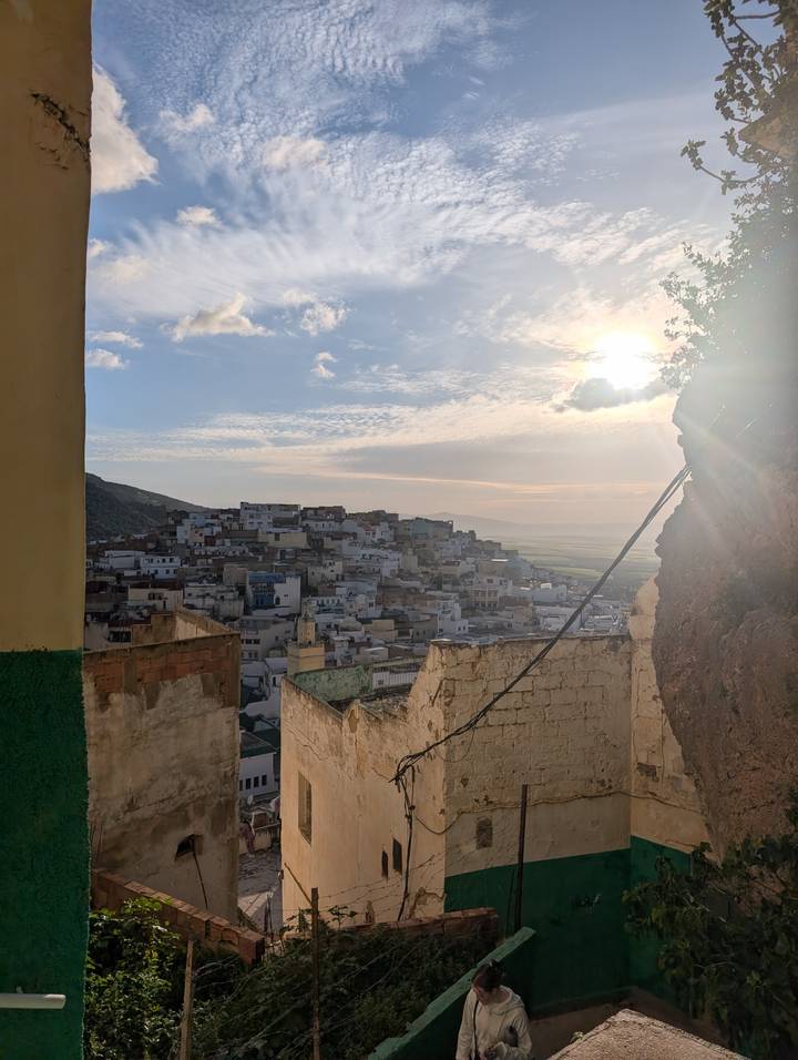 View through ruined walls toward a hillside town bathed in late-day sun with distant plains beyond.