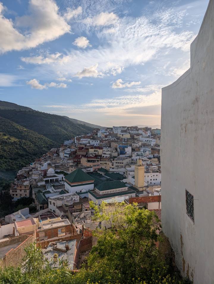 Hillside town of tightly packed pastel and blue houses framed by green mountains under soft sky.