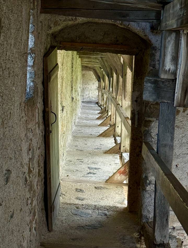 A narrow stone corridor inside a medieval castle displays rugged beams and worn walls.