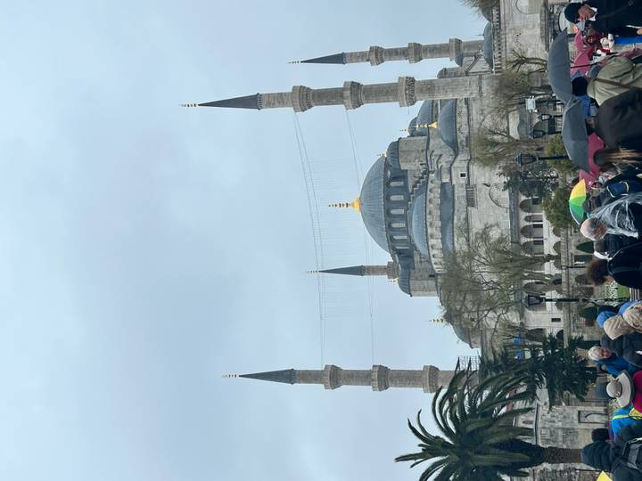 View of the Blue Mosque with crowds and umbrellas under an overcast sky.