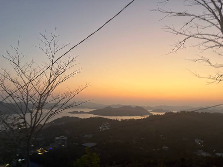 Blurred dusk view of island-dotted bay from a hillside with power lines.