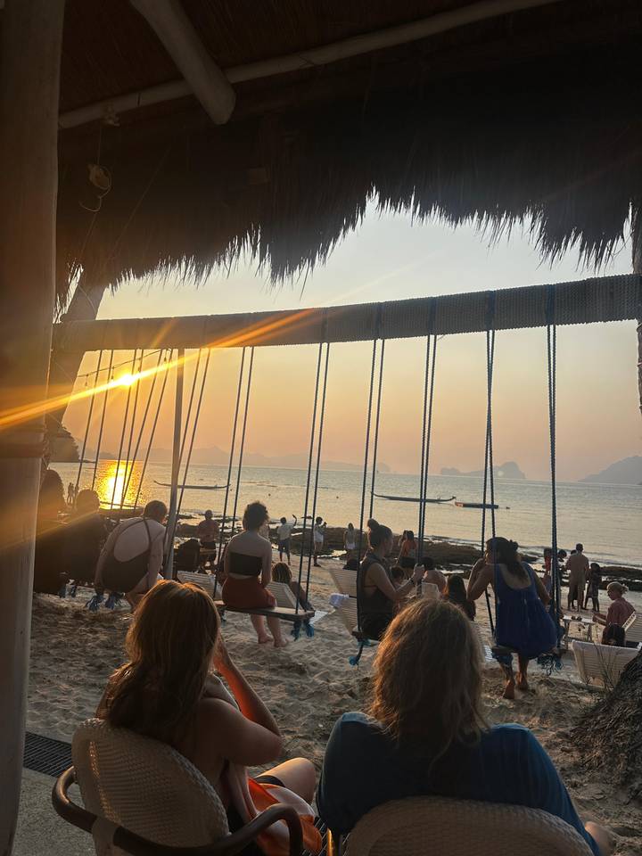 Crowded beach swing bar at sunset with golden light on the water.