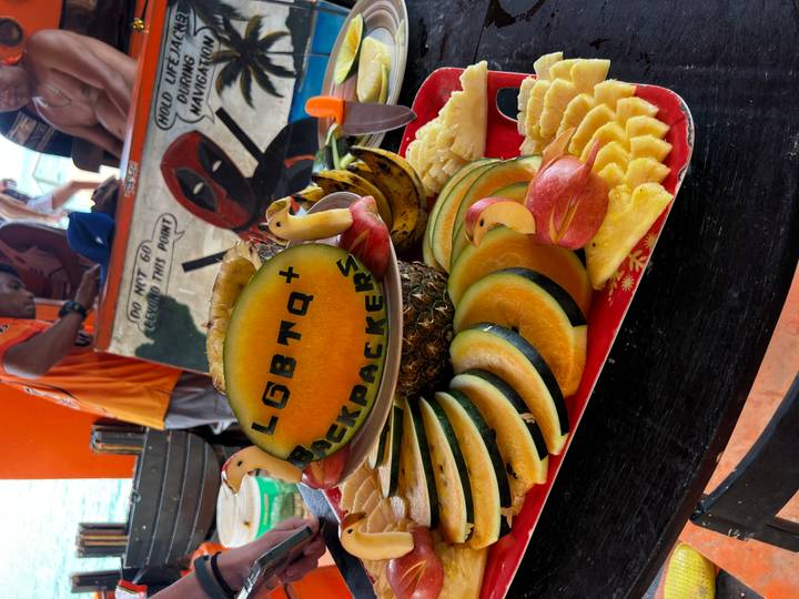 Colourful fruit platter carved with 'LGBTQ+ Backpackers' aboard a boat.