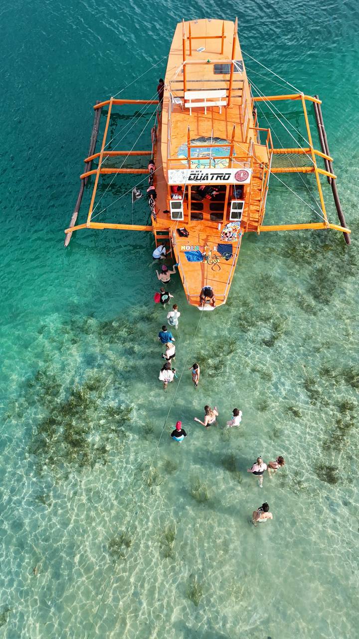 Aerial shot of travellers wading from an outrigger boat into turquoise shallows.