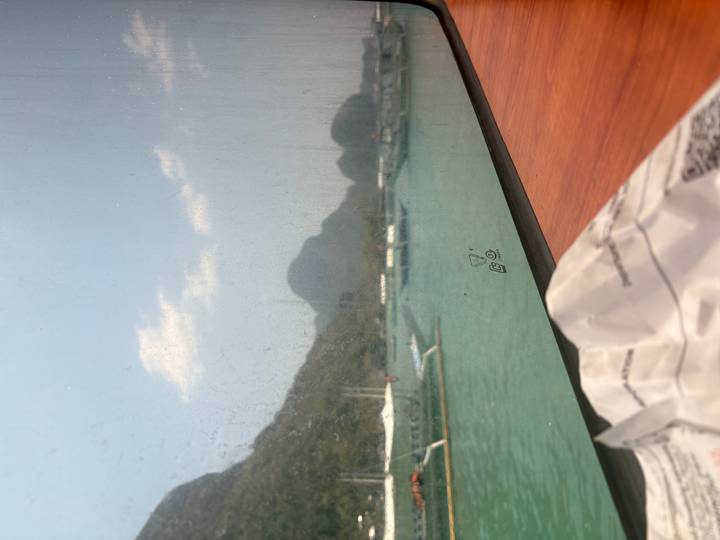 View through a dirty ferry window of green water and distant karst peaks, with a snack bag on the sill.