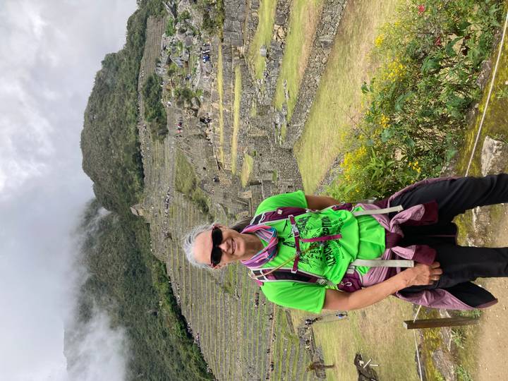 Smiling trekker stands before the terraced stone ruins of Machu Picchu under misty peaks.