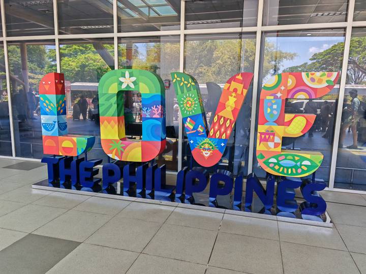 Bright multicoloured 'LOVE THE PHILIPPINES' installation outside a modern glass building.