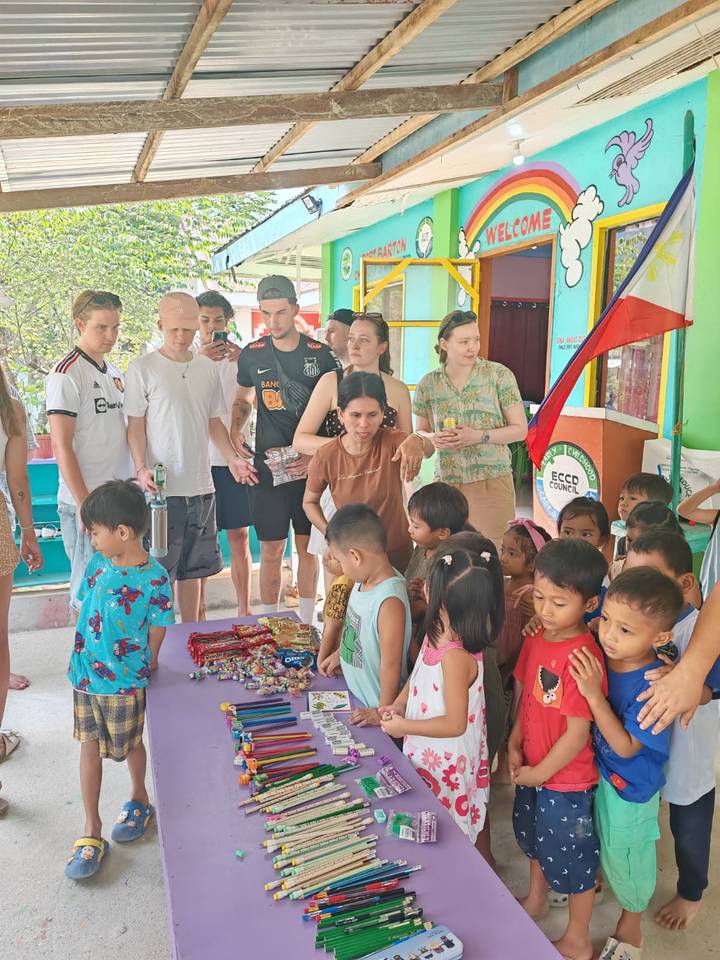 Travellers distribute snacks to local children inside a brightly painted community building.