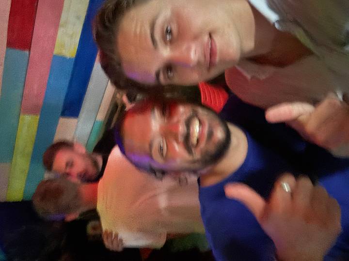 Blurry nightlife selfie of two men giving thumbs-up inside a colourful bar.