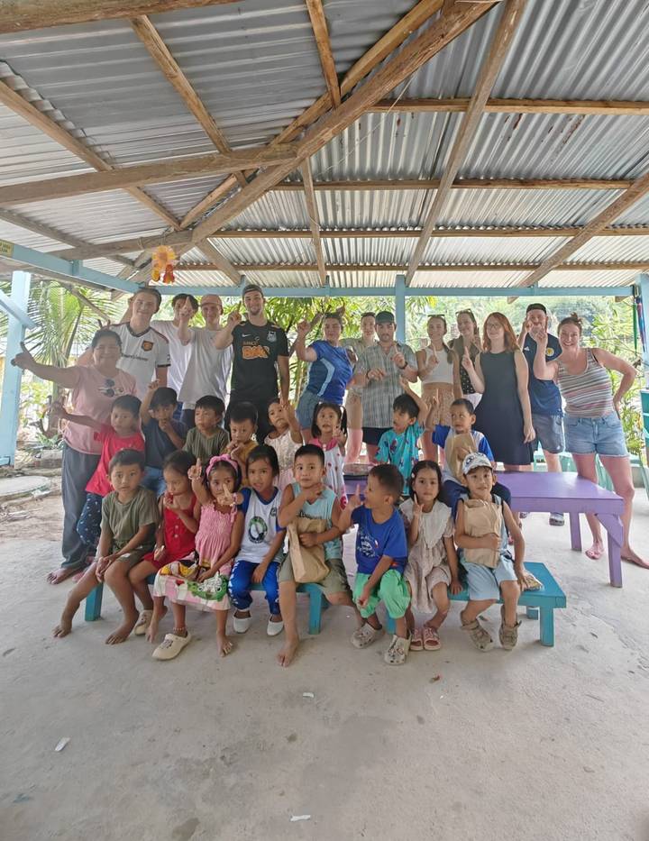 Tour group and local children smiling together for a keepsake photo in a shaded meeting area.
