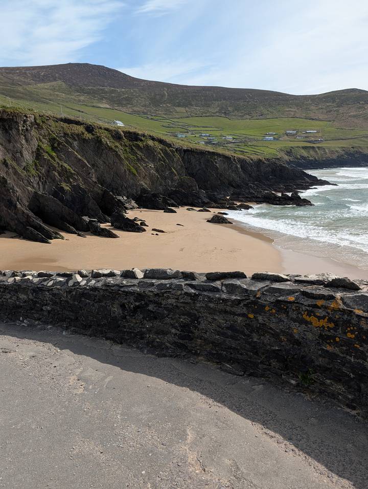 Secluded sandy cove with crashing Atlantic waves below rocky cliffs in Ireland.
