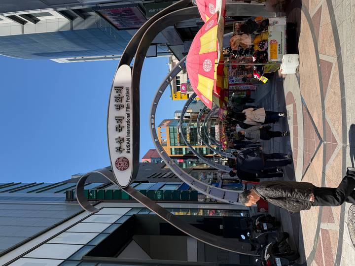 Crowds enter the BUSAN International Film Festival street under modern archways.