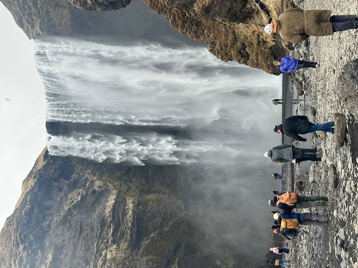 Visitors walk at the base of the towering Skogafoss waterfall amid spray and cliffs.
