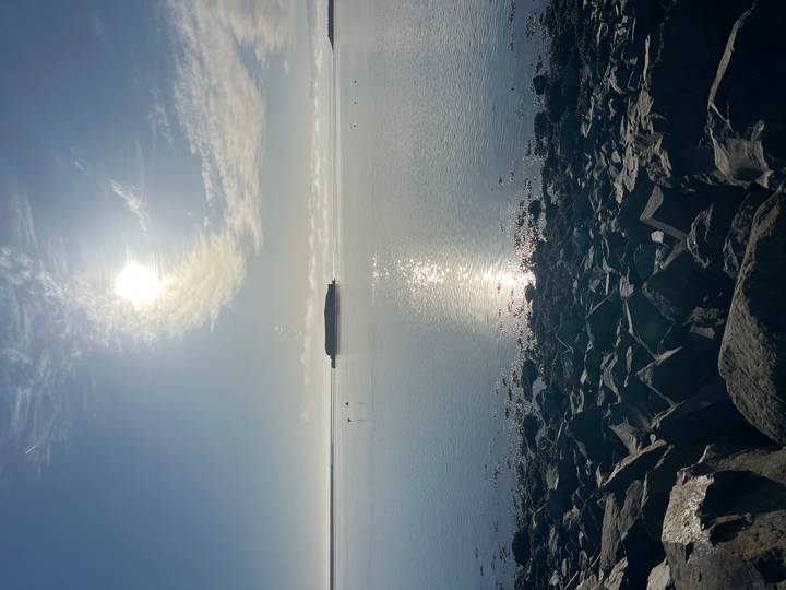 Low sun glistens over calm coastal waters and a rocky shoreline.