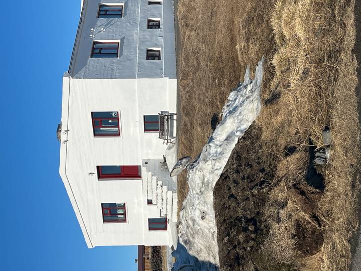 Simple white farmhouse with red trim set against dry grass and lingering snow.