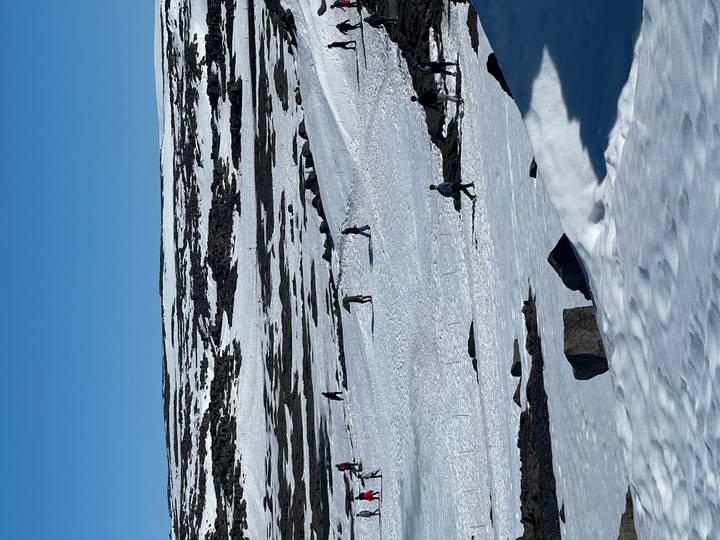 Travellers walk across a vast snowy landscape dotted with rocks and fences.