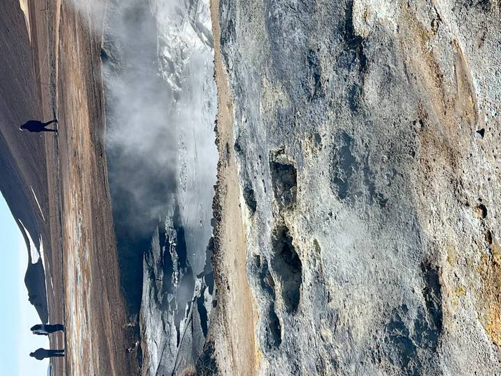 Steaming geothermal mud pool and mineral crusts at Namaskard with lone visitor above.