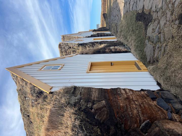 Row of traditional turf-roofed cottages built into a rocky hillside under blue sky.