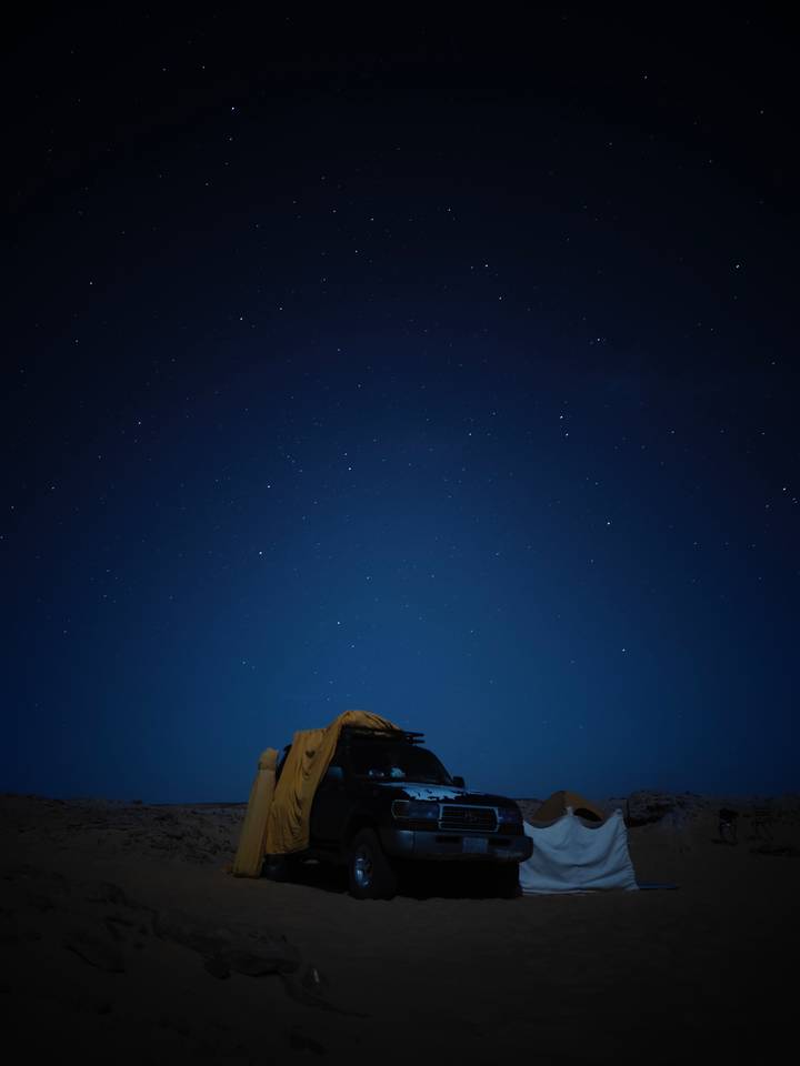 Star-filled night sky above a low desert camp silhouette