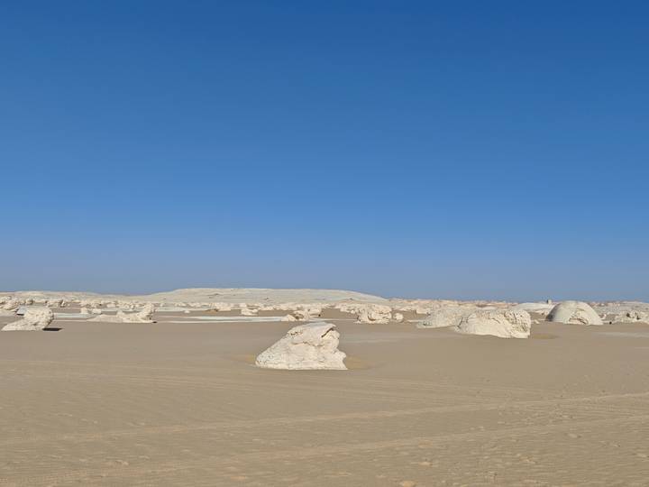 Surreal white limestone formations dotting an expansive desert under cloudless blue skies