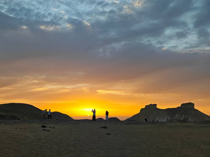 Tourists silhouetted against a vivid desert sunset with rocky buttes on the horizon