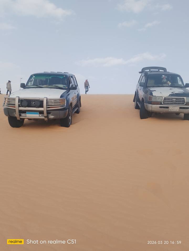 Two jeeps atop a wind-swept sand dune with tourists in the background