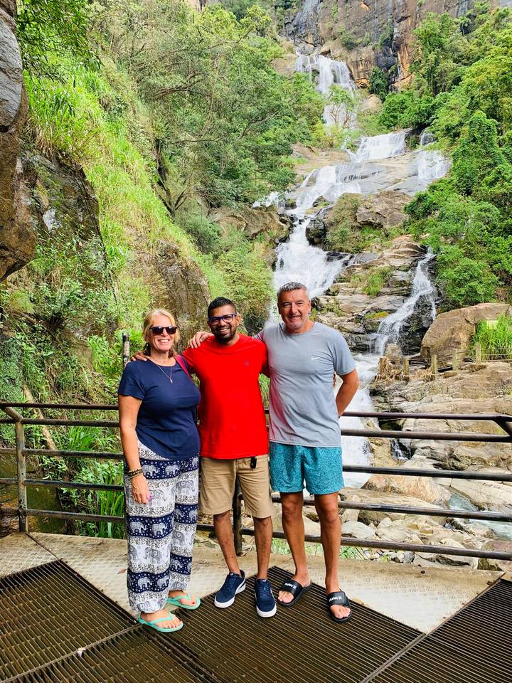 Three travellers pose together in front of a cascading jungle waterfall