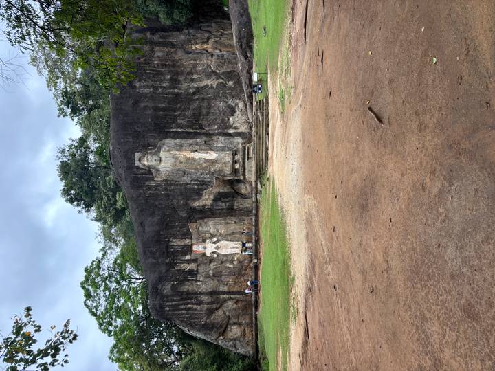 Ancient rock face with large standing Buddha carvings surrounded by greenery