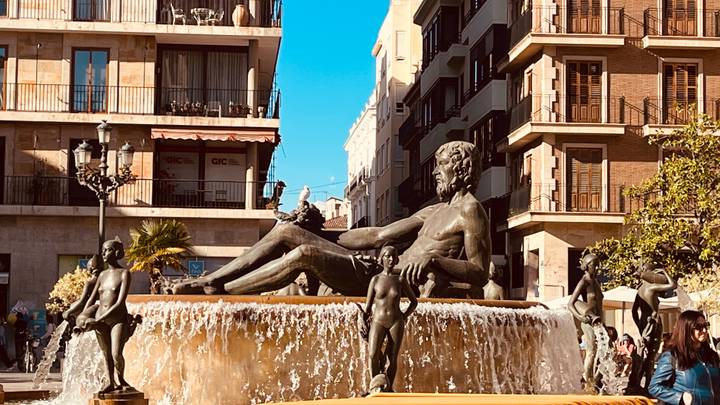 Classical fountain with reclining statue surrounded by cherubs in a lively city square
