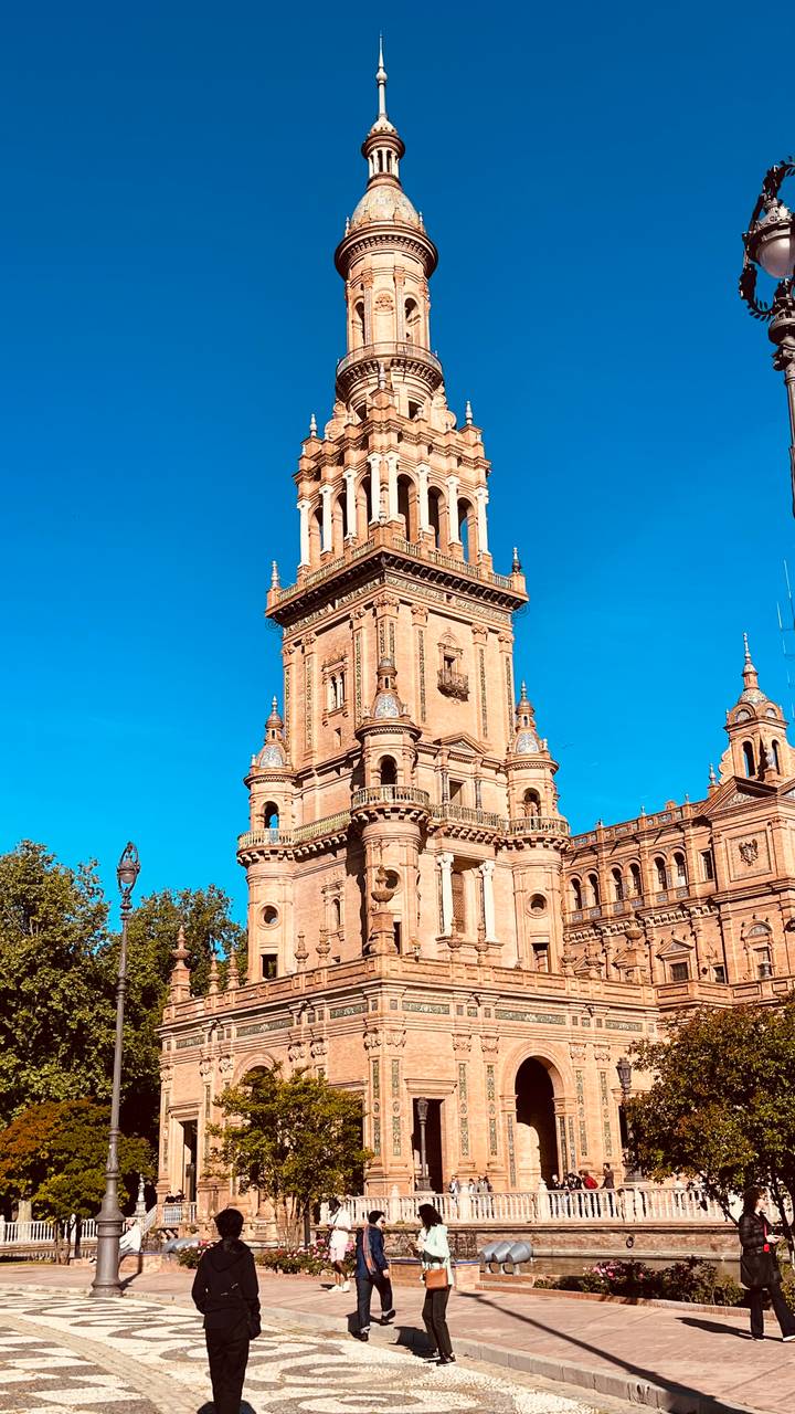 Tall ornate tower of Plaza de España rising against a clear blue sky.