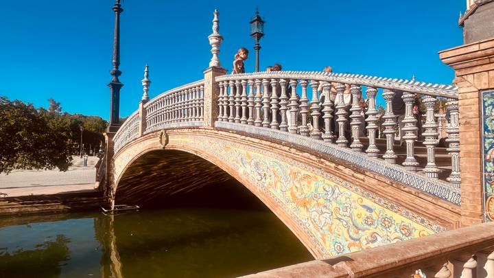 Decorative tiled bridge over a small canal with a few tourists standing on top.